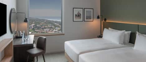 Ein Hotelzimmer mit Bett, Schreibtisch, Sessel, Fernseher und einem großen Fenster mit Blick.