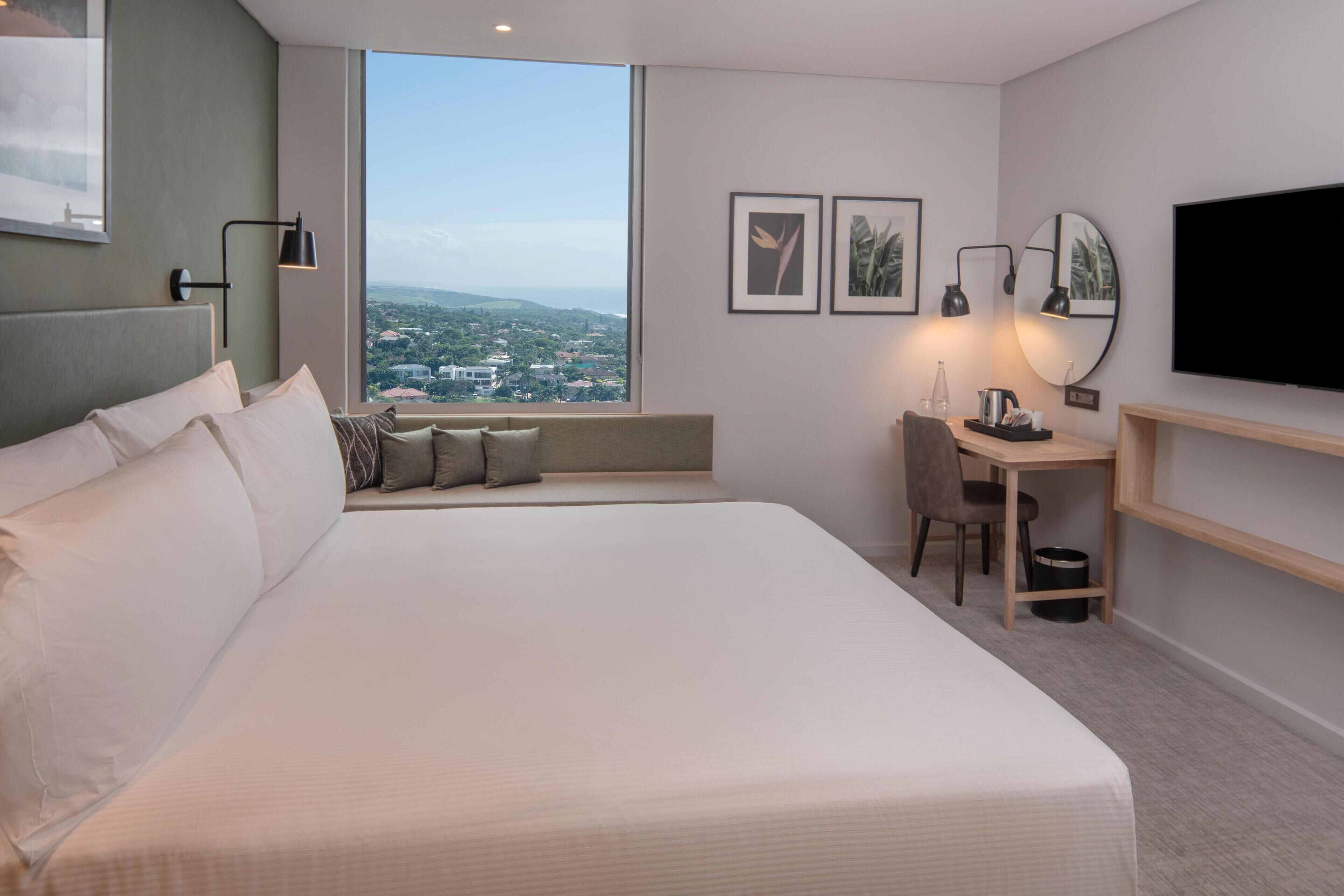 Een moderne hotelkamer met een groot bed, een bureau, een stoel, een televisie en uitzicht op de stad.