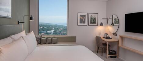 A modern hotel room with a large bed, a desk, a chair, a TV, and a view of the city.