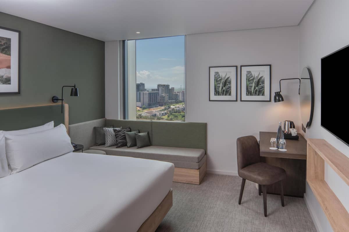 A modern hotel room with a large bed, a sofa, a desk, and a TV.
