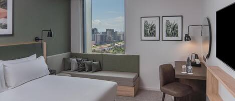 Moderni hotellihuone, jossa on suuri sänky, sohva, työpöytä ja televisio.