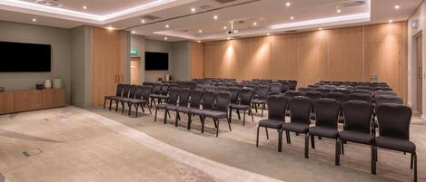 A conference room with rows of chairs, a projector screen, and a wooden panel wall.