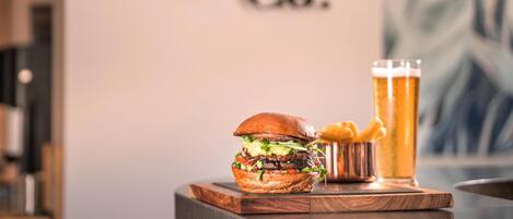 A burger, a glass of beer, and fries on a wooden board with a sign in the background.