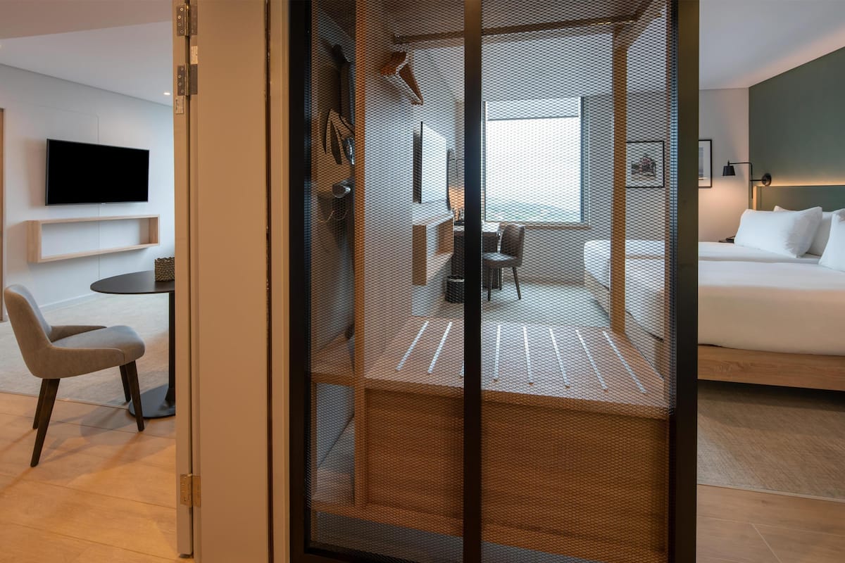 A modern hotel room with a large bed, a dining area, and a TV mounted on the wall.
