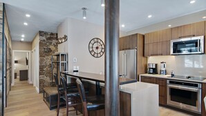 Une cuisine moderne dotée d’un îlot central, d’appareils électroménagers en acier inoxydable et d’un mur décoratif en pierre.