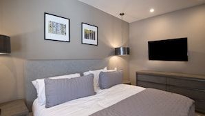 Une chambre à coucher bien rangée, avec un grand lit, deux tableaux encadrés au mur, un téléviseur fixé au mur et une lampe de chevet.