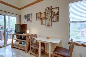 A living room with a TV on a wooden stand, a white table, and two chairs. There are four tree paintings on the wall. - 201c Mountain Side 1br 1ba 1 Bedroom Condo by RedAwning (Frisco)