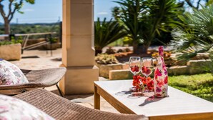 Un espace extérieur aménagé avec des meubles en osier, une table avec deux verres à vin et une bouteille, et une vue sur le paysage.
