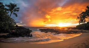 Ein Strand mit Felsen und Palmen bei Sonnenuntergang.