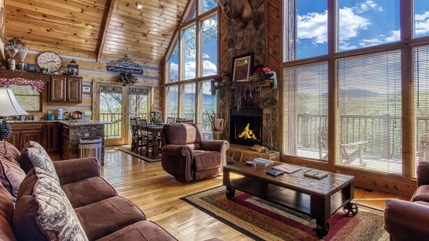 A spacious living room with a fireplace, large windows, and a stone wall. - Campfire Lodge is a beautiful cabin with all the special touches needed to make your stay memorable! (Sevierville)