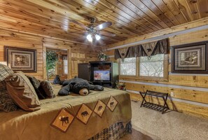 A cozy cabin room with wooden walls, a bed with a quilt, a television, and framed pictures.