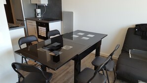 Una cocina moderna con horno empotrado, cafetera y microondas. Hay una mesa de comedor con sillas y un sofá negro en la sala de estar.