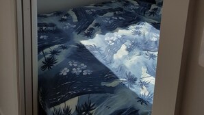 Una habitación pequeña con una cama individual, estampado tropical, ventana con vista a la playa y una puerta.