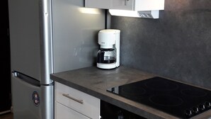 Una cocina compacta con refrigerador de acero inoxidable, cafetera, estufa y lavavajillas.