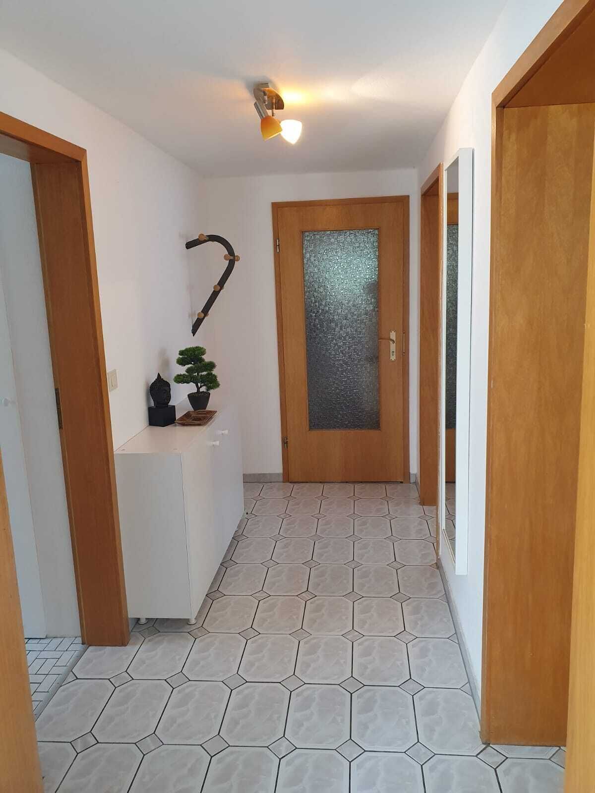 A hallway with hexagonal tiled flooring, a wooden door with a frosted glass panel, and a wall-mounted light fixture.