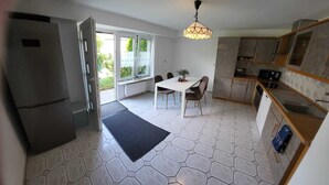 Cocina compacta con zona de comedor, refrigerador y ventana con vista a vegetación.