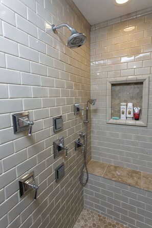 Ein Badezimmer mit Dusche, Waschtisch und Toilettenartikeln sowie einer gefliesten Wand.