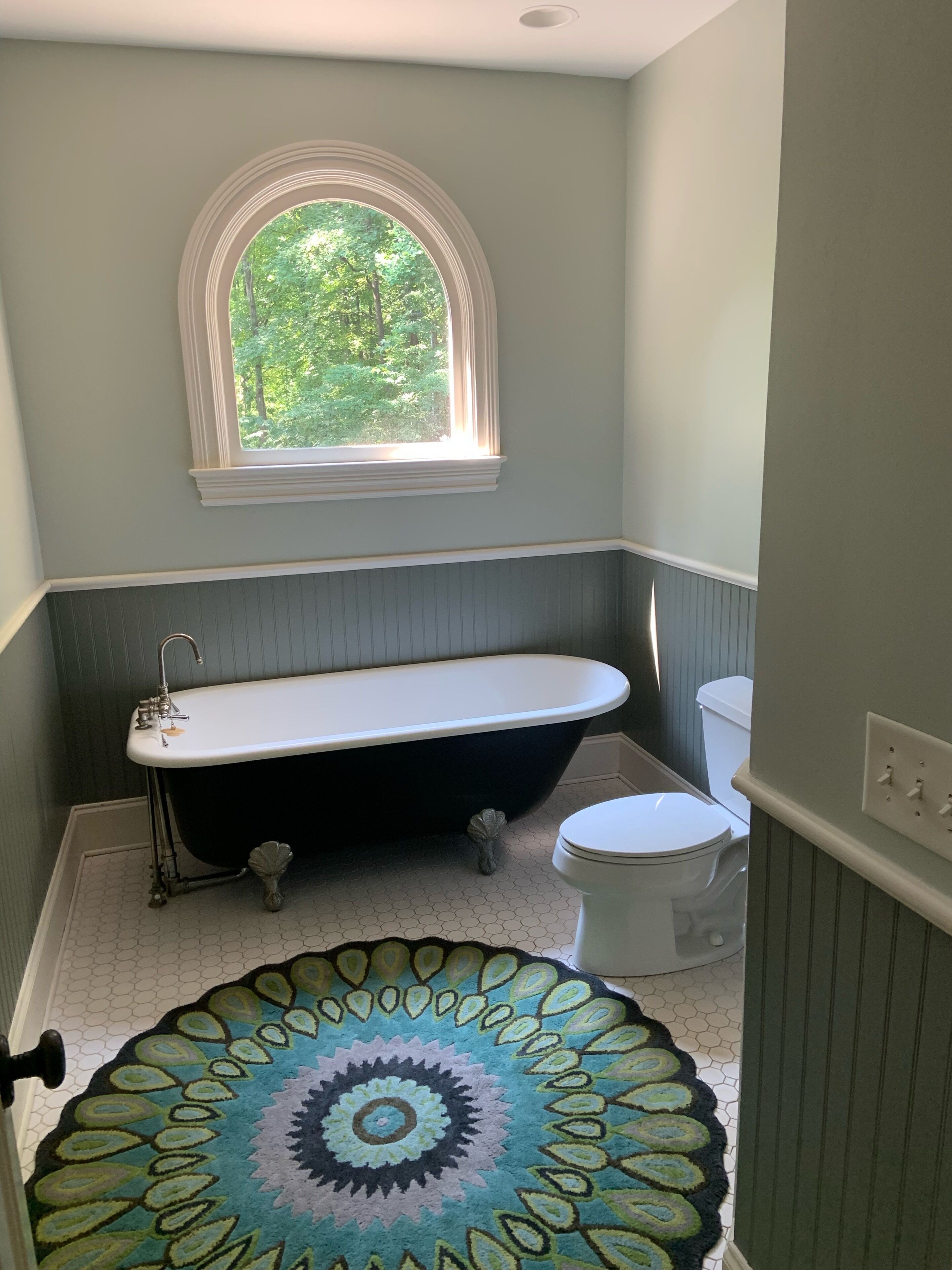 A bathroom with a freestanding bathtub, a toilet, and a window with a view of greenery.