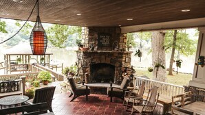 A covered patio with a stone fireplace, outdoor seating, and a view of a lake. - Beautiful Charlotte Lake Wylie Waterfront Bungalow (Charlotte)