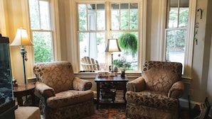A cozy living room with two patterned armchairs, a small table with a lamp, and a large window with a view of greenery. - Beautiful Charlotte Lake Wylie Waterfront Bungalow (Charlotte)