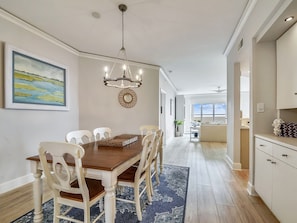 A dining area with a wooden table, white chairs, a chandelier, and a painting on the wall.