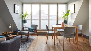 A modern living room with a dining area, large windows, and potted plants.