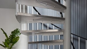 A spiral staircase with a white railing, a teal plant in a pot, and a white cabinet against a blue wall.