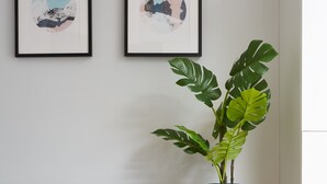 A modern living room with a grey sofa, two blue cushions, a potted plant, and two framed abstract artworks on the wall.
