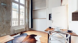 A modern kitchen with a wooden table, white chairs, and a cowhide rug. - Chez Gustave: AC Calm, Saint Paul Marais, 2Guests (Paris)