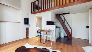 A modern kitchen with white cabinets, a wooden dining table, and a staircase leading to an upper level. - Chez Gustave: AC Calm, Saint Paul Marais, 2Guests (Paris)