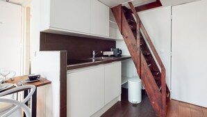 A modern kitchen with white cabinets, a wooden staircase, and a dining area with a table and chairs. - Chez Gustave: AC Calm, Saint Paul Marais, 2Guests (Paris)