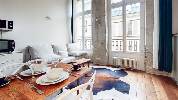 A cozy living room with a wooden dining table set for two, a sofa, and a stone wall. - Chez Gustave: AC Calm, Saint Paul Marais, 2Guests (Paris)