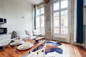 Un salon chaleureux avec une table à manger en bois, dressée pour deux personnes, un canapé et un mur en pierre.