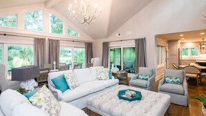 Un ampio soggiorno con soffitto alto, ampie finestre e un lampadario. Sono presenti diverse zone relax con divano, poltrone e tavolino.