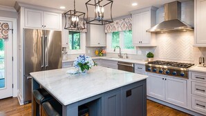 Una cucina moderna con mobili bianchi, un frigorifero in acciaio inossidabile, un piano cottura a gas e illuminazione a sospensione.