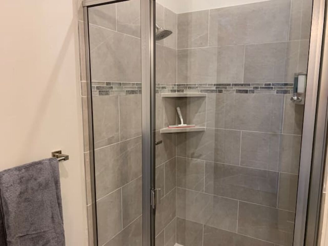 A glass-enclosed shower with grey tiles and a small shelf.