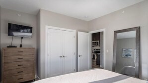 Une chambre avec un lit, une commode, un téléviseur, une armoire et un coin cuisine.