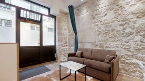 Ein modernes Wohnzimmer mit Steinwand, einem braunen Sofa, einem weißen Couchtisch und Blick ins Freie durch ein großes Fenster.