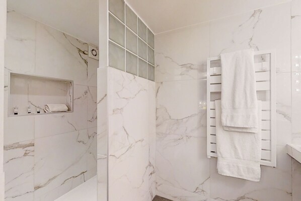A bathroom with marble walls, a glass shower enclosure, and a white towel rack. - Loft Heart of Paris, Marais, Chatelet, Beaubourg (Paris)