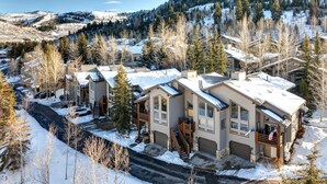 A residential area with modern houses, a road, and a snowy landscape with trees and hills in the background.