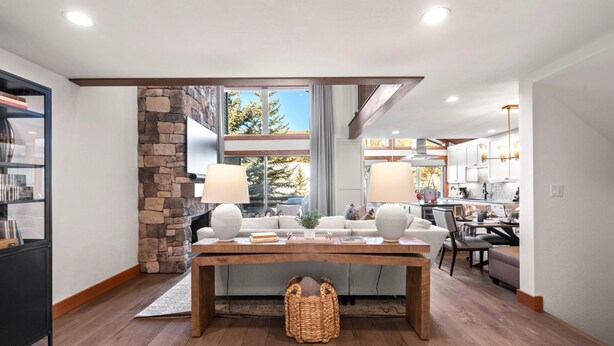A modern interior with a stone fireplace, a dining area with a wooden table, and a kitchen in the background.