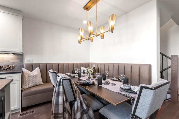Un espace de salle à manger moderne, doté d’une longue table, de bancs rembourrés et d’un lustre contemporain.