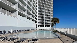 A poolside area with sun loungers, a clear blue sky, and a tall building with balconies. - Direct Gulf front, sea breeze! - 3BR/3BA - Lighthouse 1115 - Spectacular views!  (Gulf Shores)