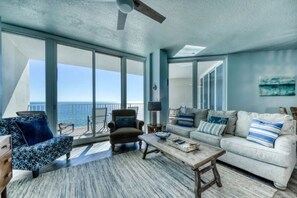 Relax in this spacious living room with a high ceiling and ceiling fan, featuring a large sliding glass door leading to a balcony with ocean views.