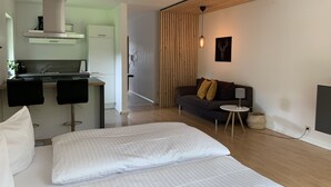 A modern, well-lit room with a bed, a sofa, a small table, and a kitchenette. - Ferienwohnung am Ententeich (Bad Marienberg)