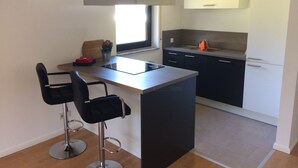 A modern kitchen with a central island, two bar stools, a window, and a built-in oven. - Ferienwohnung am Ententeich (Bad Marienberg)