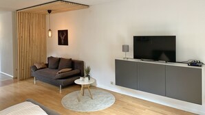 A modern living room with a grey sofa, a round coffee table, a flat-screen TV on a grey cabinet, and a wooden slatted wall. - Ferienwohnung am Ententeich (Bad Marienberg)