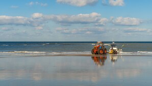 Une plage avec un tracteur et un petit bateau près du bord de l’eau.