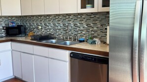 A modern kitchen with white cabinets, a stainless steel refrigerator, a dishwasher, and a tiled backsplash.