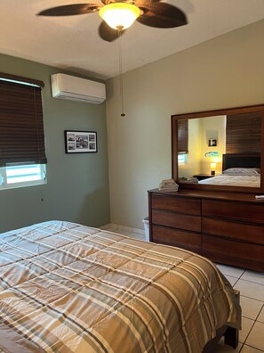 Un dormitorio con cama, cómoda, ventilador de techo, aire acondicionado instalado en la pared y un cuadro enmarcado.